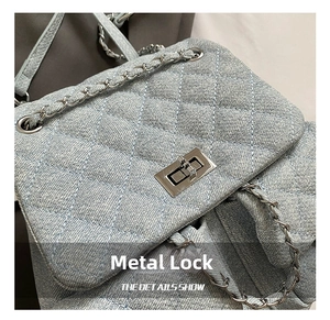 Detail of denim quilted backpack featuring silver twist lock and metal chain strap