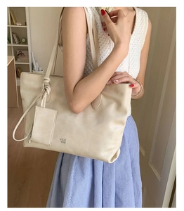 Detail of a large cream tote bag with attached small card pouch and knot handle design