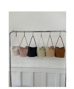 Detail view of woven bucket bags in six colors hanging on a minimalist chrome rack