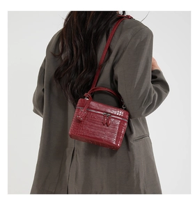 Close-up of deep red crocodile pattern handbag featuring silver dual zippers and studs