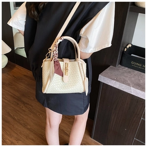 Détail du sac seau tressé crème avec foulard en soie décoratif et fermoir métallique