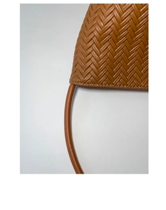 Close-up detail of premium caramel brown woven leather texture and curved handle