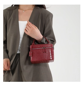 Detail of burgundy crocodile pattern handbag with dual zippers and handle on model