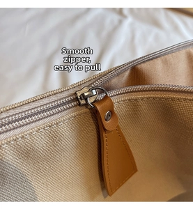 Dettaglio della cerniera in metallo e tiralampo in pelle marrone sulla borsa in tela beige