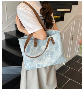 Detail of light blue canvas tote bag with brown leather straps in a casual indoor setting