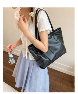 Detail of a black large-capacity soft leather tote bag with a white flower charm and straps