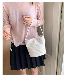 Detail of cream white woven bucket bag showing premium texture and shoulder strap