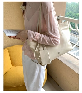 Chic cream white leather tote bag with matching small zip pouch on a soft yellow sofa