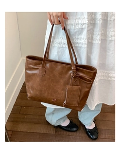 Detail of caramel brown tote bag with knot design and hanging pouch on white dress