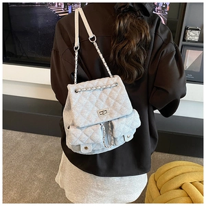 Detailed view of quilted denim backpack with metal lock and chain strap on model back