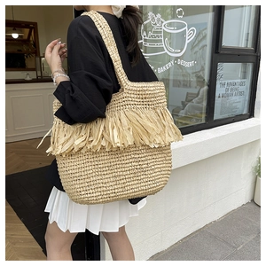 Fashionable khaki woven straw tote bag with fringe detail shown in an outdoor street setting