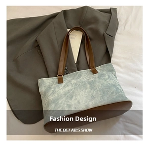 Detail of blue washed canvas tote with brown leather straps on a white background