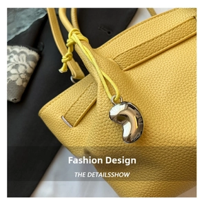 Detail of yellow lychee grain leather bucket bag with silver bean-shaped metal pendant