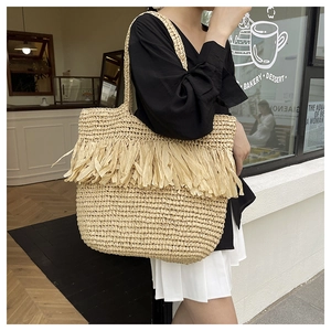 Detail of hand-woven straw tote bag with fringe tassels and natural raffia texture