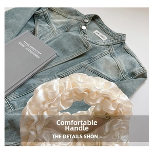 Close-up of pleated satin ruffles on a creamy white handbag over a denim jacket