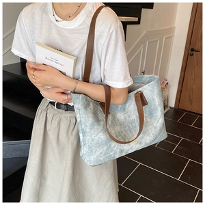 Detail of light blue tie-dye tote bag with brown leather handles worn by model