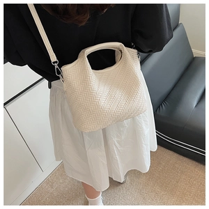 Detail of cream woven handbag with V-shaped texture and detachable shoulder strap on model