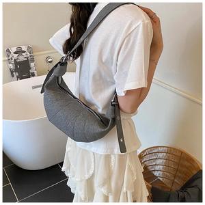 Detail shot of a grey fabric crossbody crescent bag showing the minimalist pleats and strap
