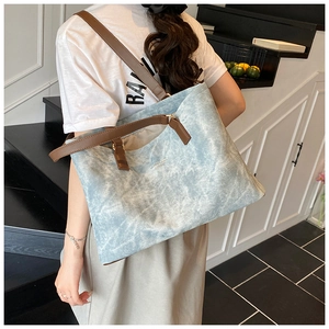 Close-up of light blue canvas tote bag with brown leather straps and gold logo detail