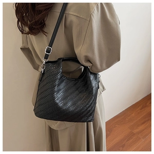 Detail of black woven bucket bag showing leather texture and detachable shoulder strap