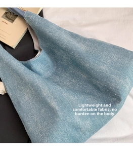 Macro detail of a light blue denim tote bag with silver studs and soft fabric texture