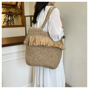 Close-up of handmade woven straw tote bag with fringe details on a female shoulder