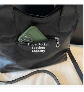 Close-up of a black leather tote bag showing the front zipper pocket with a phone for scale