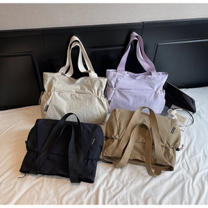 Detail of four colorful nylon tote bags with adjustable side drawstrings on a white bed