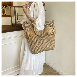Detail of hand-woven straw tote bag with fringe accents and textured cylindrical handles