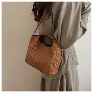 Brown woven bucket bag showing dual handles and shoulder strap texture on a model