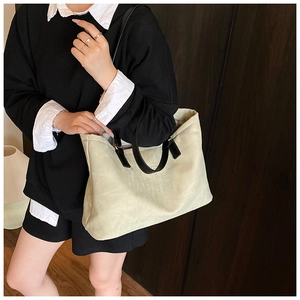 Detail of light green canvas tote bag with black leather handles and metal hardware