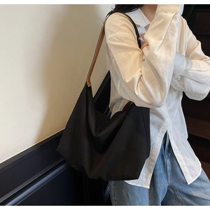 Dettaglio borsa tote in tela nera minimalista con manici in pelle marrone a spalla