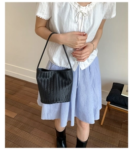 Detailed view of a black woven bucket bag with elegant thin handle and leather texture