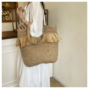 Detail van bohemien geweven strooien draagtas met decoratieve raffia kwastjes en riemen