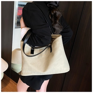 Detail of a large khaki textured tote bag with black leather handles held by a model