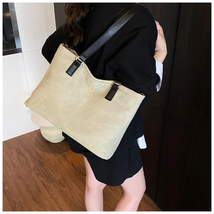 Close-up of beige tote bag featuring black leather strap and gold embossed lettering