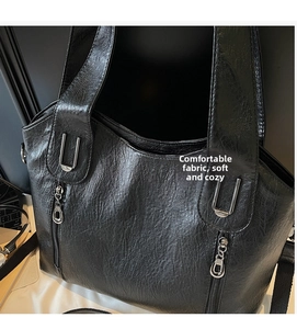 Close-up of black leather tote bag with silver U-shaped metal rings and zip pockets
