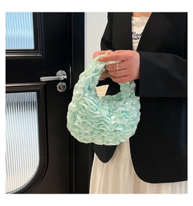 Detail of mint green ruched cloud handbag with satin texture on black suit outfit
