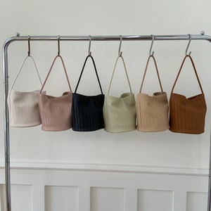Detail view of woven bucket bags in various colors hanging on a minimalist metal rack