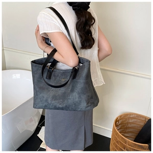 Grey washed canvas tote bag with black straps shown on shoulder for size reference
