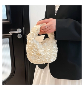 Close-up of ruffled cream satin handbag showing layered pleats and a soft handle