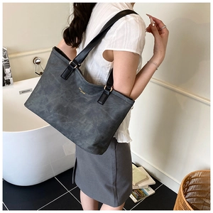 Detail of grey tote bag with black leather strap and golden ring buckles shown on model