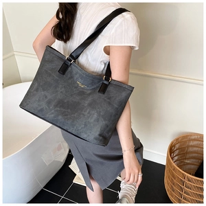 Detail of grey suede tote bag with black leather handles and gold metal hardware