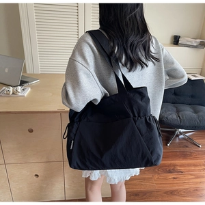 Close-up of black oversized nylon tote bag with drawstring detail and minimalist side label