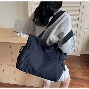 Detail view of large black nylon tote bag featuring wide strap and side drawstring pocket