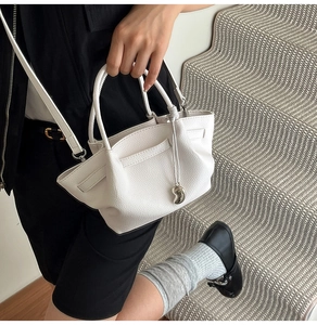 Close-up of white lychee grain leather bucket bag with silver heart charm and soft folds
