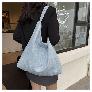 Side view of a large light blue denim tote bag worn by a model in a cafe setting