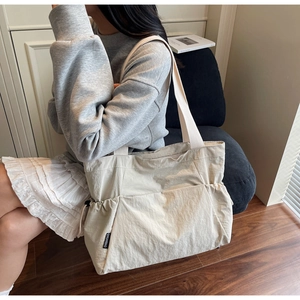 Detail of beige nylon tote bag featuring functional side drawstring pocket and brand label