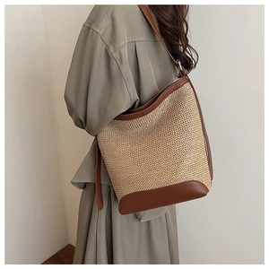 Détail d'un grand sac bandoulière en paille avec bordure en cuir marron sur modèle