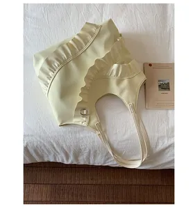 Detailed top view of a cream ruffled shoulder bag on white bedding with a French book
